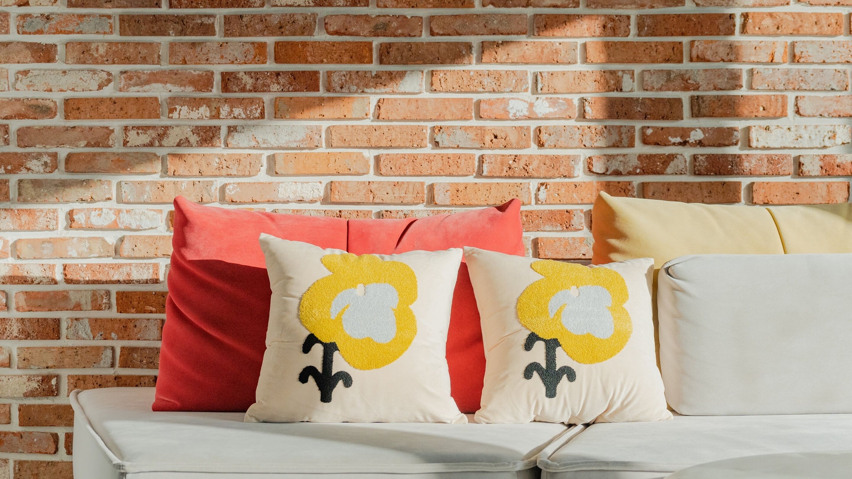 A white sofa with three pillows against a brick wall.