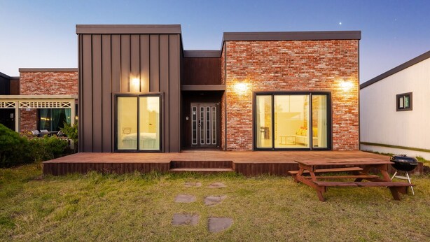 A modern house with a brick facade, large sliding glass doors, and a wooden deck. - Jeju Pureunbada Pet Dokchae Pension (Jeju City)