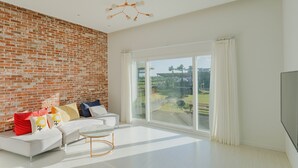 A modern living room with a white sofa, a round coffee table, and a brick wall. - Jeju Pureunbada Pet Dokchae Pension (Jeju City)