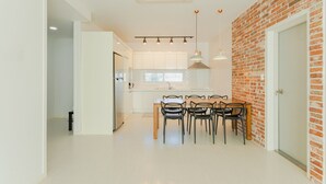 A modern kitchen with white cabinets, a brick accent wall, and a dining area with four chairs. - Jeju Pureunbada Pet Dokchae Pension (Jeju City)