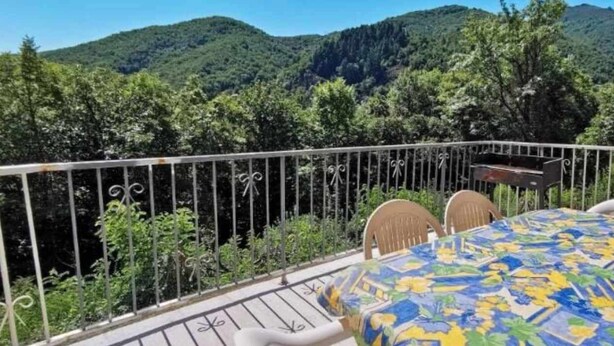 A balcony with a table and chairs, surrounded by a metal railing, overlooking a mountainous landscape.