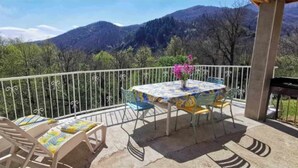 A balcony with a table and chairs, a flower vase, and a mountain view.