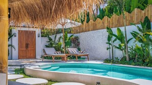 A pool area with lounge chairs, a wooden door, and a thatched roof structure. - Malta Villa by Betterplace (Ubud)