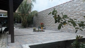 Um pátio com parede de tijolos, palmeiras e um pequeno jardim com plantas em vasos.