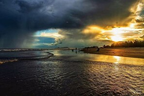 Een strand met een ondergaande zon, kalm water en een verre kustlijn.
