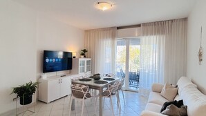 Ein modernes Wohnzimmer mit einem Flachbildfernseher, einem Esstisch mit Stühlen, einem Sofa und einer Glastür zum Balkon.