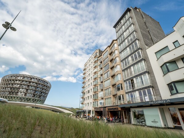 A modern building with a unique spherical structure, a multi-story residential building, and a commercial area with shops. - Ravenna 902 with seaview by Interhome (Middelkerke)