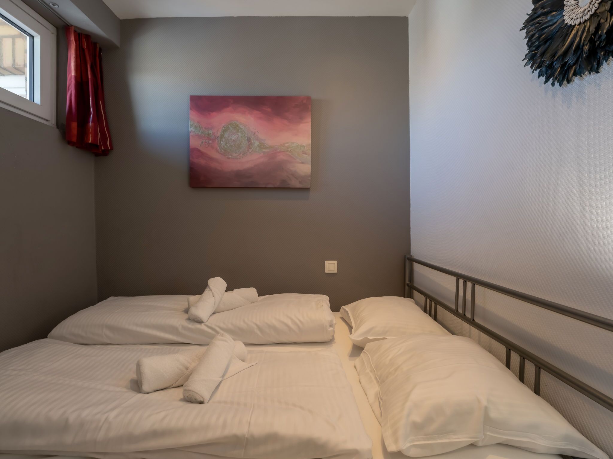 Quarto de hotel com uma cama, um quadro na parede e uma janela com cortinas.