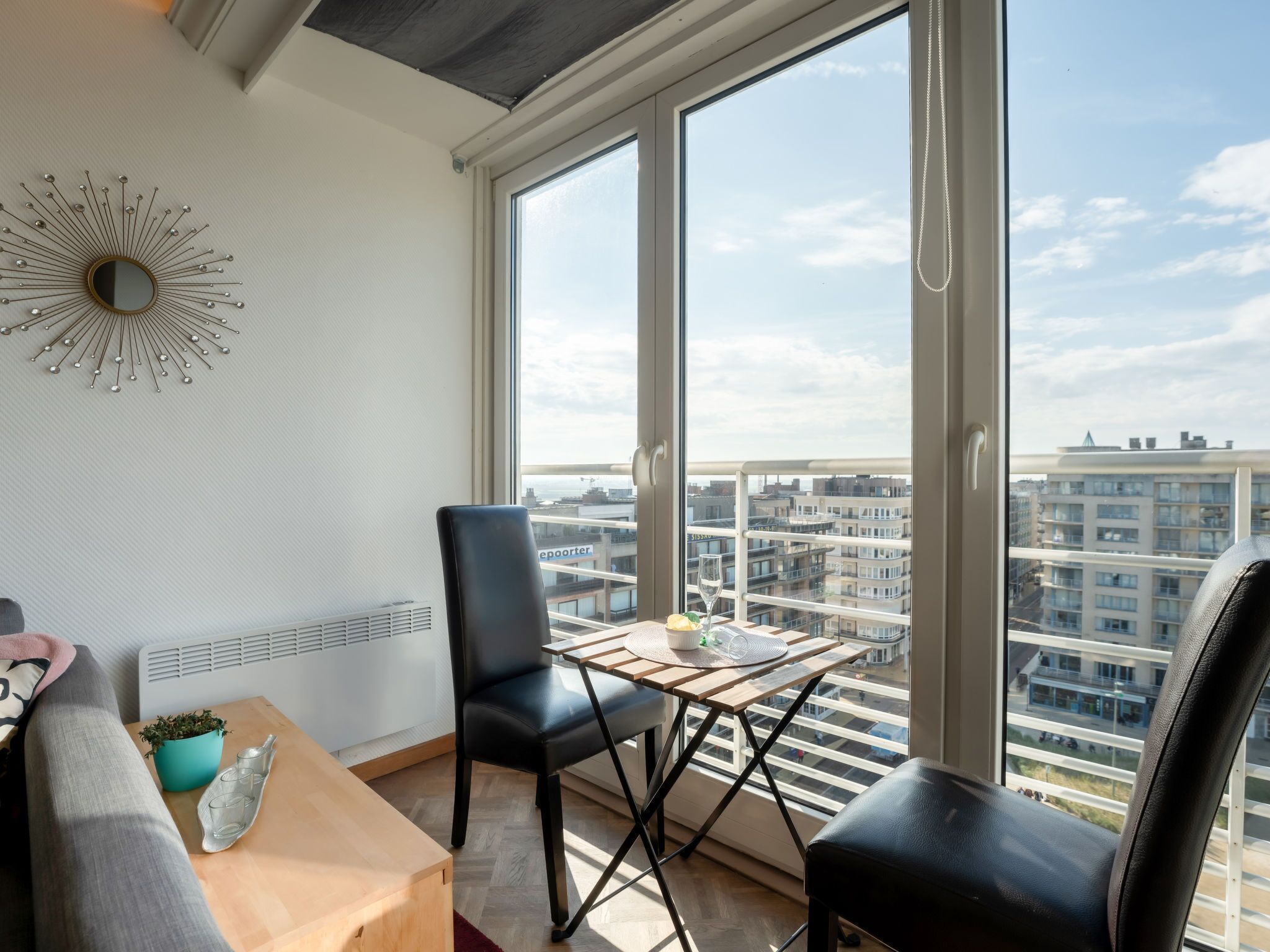 Eine moderne Wohnung mit einem großen Fenster, einem schwarzen Ledersessel, einem Holztisch und einem dekorativen Spiegel an der Wand.