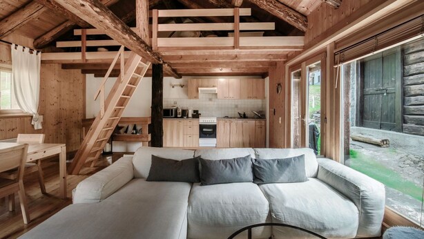 Interior de una cabaña de madera con sofá, mesa de comedor y zona de cocina.