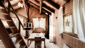Interior de una cabaña de madera con mesa de comedor, sillas, una cocina y una escalera.