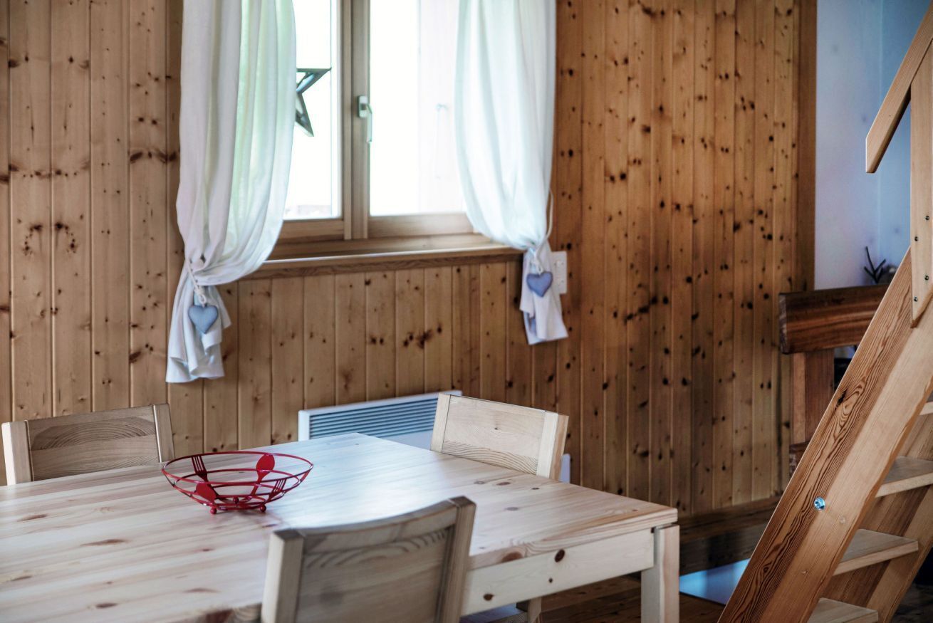 Une pièce aux murs lambrissés, comprenant une table à manger, des chaises et une fenêtre avec des rideaux.