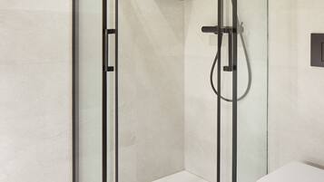 Une salle de bain moderne avec une douche à parois de verre, des toilettes et une petite étagère.