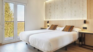 Une chambre d’hôtel moderne avec deux lits, une grande fenêtre donnant sur la verdure et un luminaire fixé au mur.