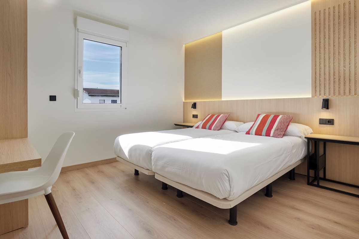 A modern bedroom with a double bed, bedside tables, a desk, and a chair.
