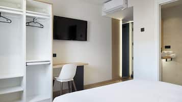 A hotel room with a bed, a desk, a chair, a wardrobe, and a TV.
