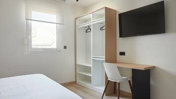 A bedroom with a bed, a desk with a chair, a wardrobe, and a TV mounted on the wall.