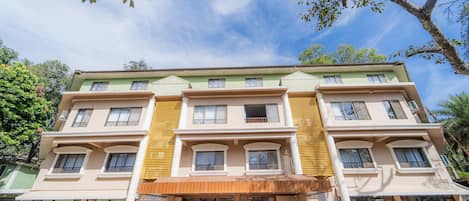 Un immeuble à plusieurs étages doté d’une entrée centrale, de balcons et de plantes en pot.