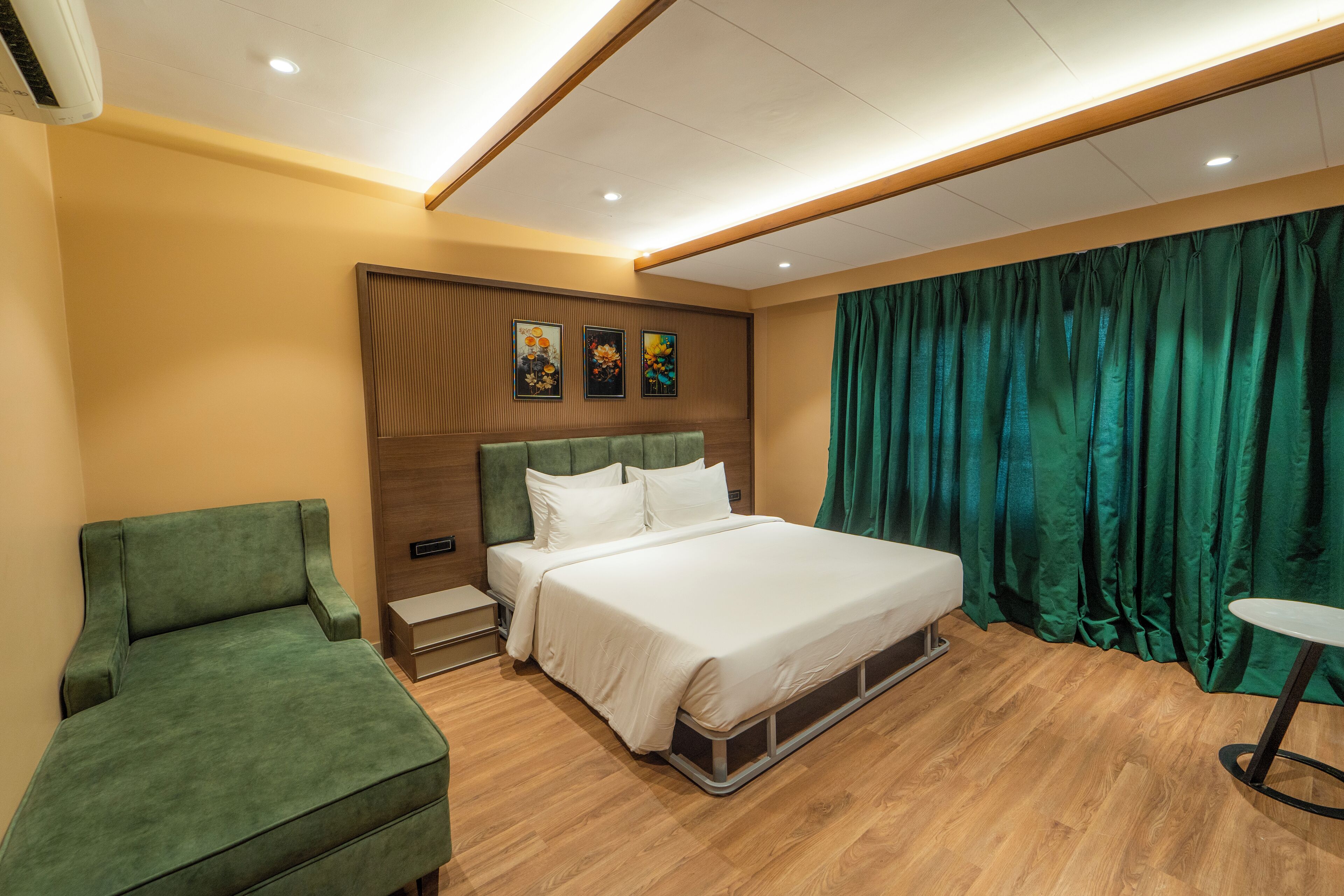 Een moderne hotelkamer met een bed, een groene fauteuil, een klein tafeltje en een houten hoofdbord.