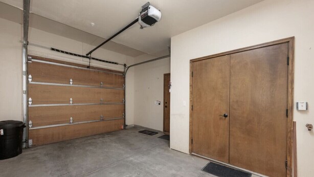 A garage with a closed wooden door, a concrete floor, and a ceiling-mounted security camera.