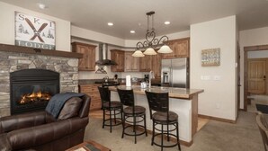 A modern kitchen with a stone fireplace, wooden cabinets, and a bar area with stools. - Hot Tub | Mountain Views | Steps to Trails (Winter Park)