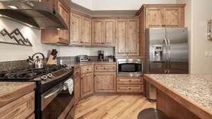 A modern kitchen with wooden cabinets, stainless steel appliances, granite countertops, and a visible stove. - Hot Tub | Mountain Views | Steps to Trails (Winter Park)