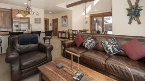 A spacious living area with a brown leather sofa, wooden coffee table, and pendant lighting.