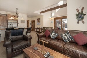 A spacious living area with a brown leather sofa, wooden coffee table, and pendant lighting. - Hot Tub | Mountain Views | Steps to Trails (Winter Park)
