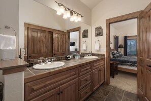 Un baño con dos lavamanos, muebles de madera, un espejo grande y una cama en la habitación contigua.