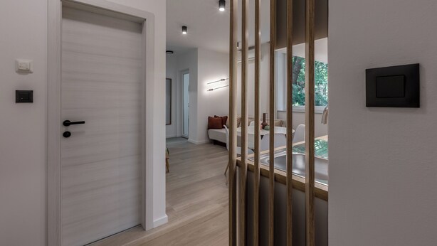 Un interior moderno con una puerta cerrada, un separador de madera y una vista parcial de un comedor con mesa y sillas.