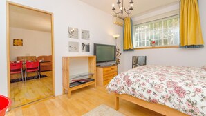 Un dormitorio con cama, televisión, ventana con cortinas y puerta que da a un comedor.