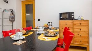 Un comedor con una mesa negra, sillas rojas y un mueble de madera con microondas.