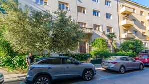 Un estacionamiento con un SUV plateado, un coche rojo y un edificio con varios balcones y ventanas.