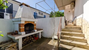 Une cour avec un four en briques, des marches menant à une porte et une chaise blanche.