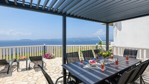 Une terrasse extérieure avec une table dressée pour le repas, offrant une vue panoramique sur la mer et les îles lointaines.