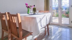 Un comedor con una mesa dispuesta para dos personas, un florero verde con flores y una botella de aceite de oliva.