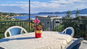 Un balcón con mesa y sillas, que ofrece vistas de la costa, con casas y colinas.