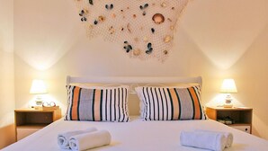 A neatly made bed with striped pillows, two bedside lamps, and a decorative shell wall hanging.