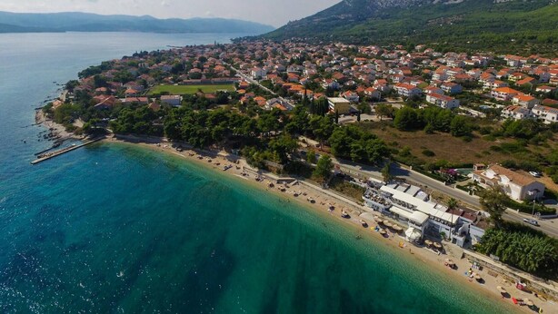 A coastal town with a beach, houses, and a mountainous backdrop.