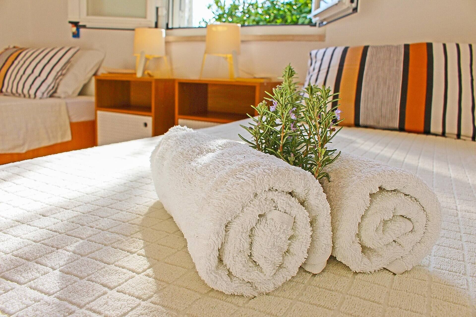 Una cama bien hecha con toallas blancas enrolladas y una pequeña planta en maceta.