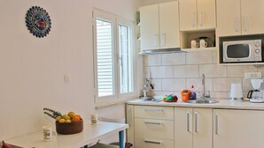 A compact kitchen with white cabinets, a microwave, a sink, and a small dining area with a red chair.