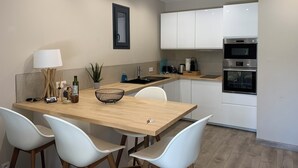 A modern kitchen with white cabinets, a wooden dining table, and two white chairs. - Seaside gîte 2 to 4 pers. (Vidauban)