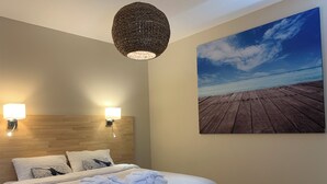 A neatly made bed with white linens and towels, two wall-mounted lights, and a large beach-themed painting on the wall. - Seaside gîte 2 to 4 pers. (Vidauban)
