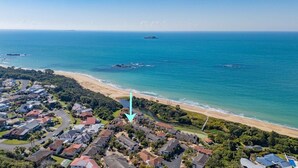 An aerial view of a coastal residential area with houses, a beach, and a clear view of the ocean.