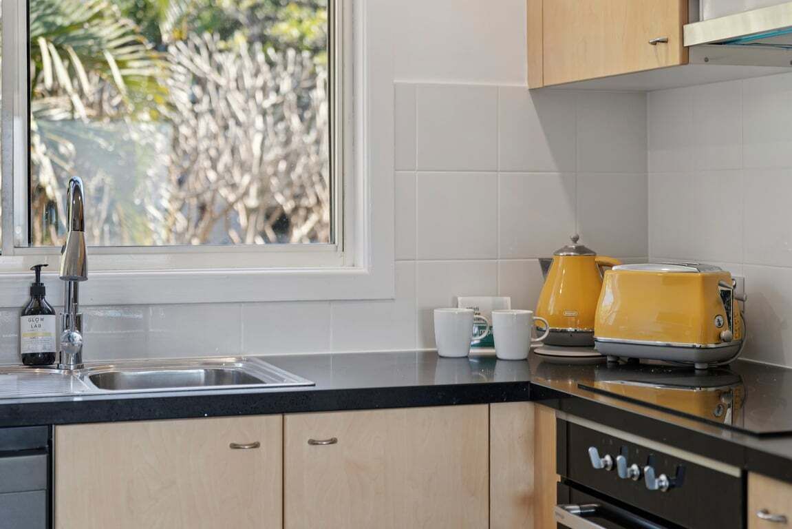 A kitchen with a window, a sink, a toaster, and a bottle of hand soap.