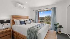 A bedroom with a wooden bed, a nightstand, a bedside lamp, a window with curtains, and a view of trees.