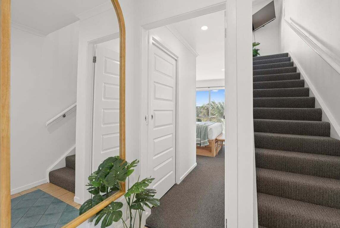 A hallway with a staircase leading to a bedroom with a bed and a window.