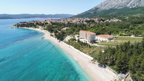 Un hotel sul lungomare con vista sulla spiaggia, un edificio grande con tetto rosso e una zona boschiva circostante.