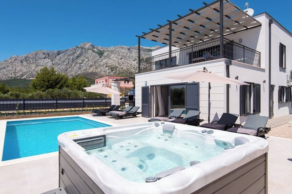 A modern villa with a swimming pool, a hot tub, and a terrace with sun loungers.