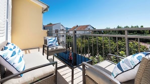A balcony with wicker furniture, a glass table, and a view of neighboring houses.